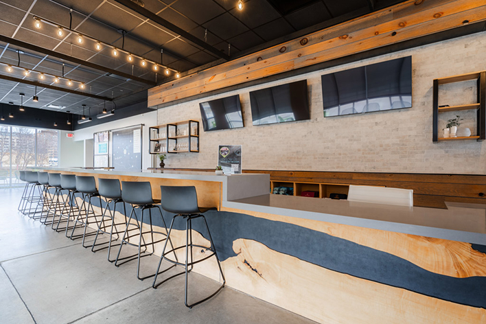 Interior bar or lounge area featuring a long wooden counter, barstools, mounted TVs, and hanging lights.