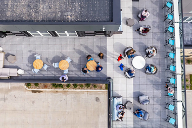 Aerial view of an outdoor rooftop patio with tables, chairs, and small groups of people gathered.