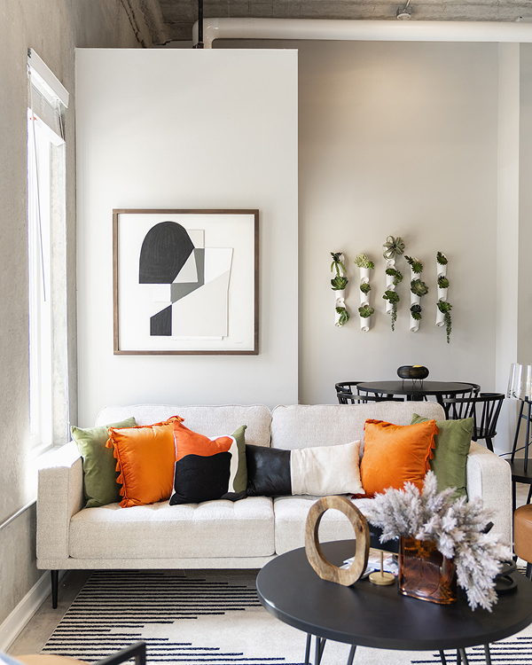 Modern living room with a light sofa, colorful pillows, abstract wall art, and a round coffee table.
