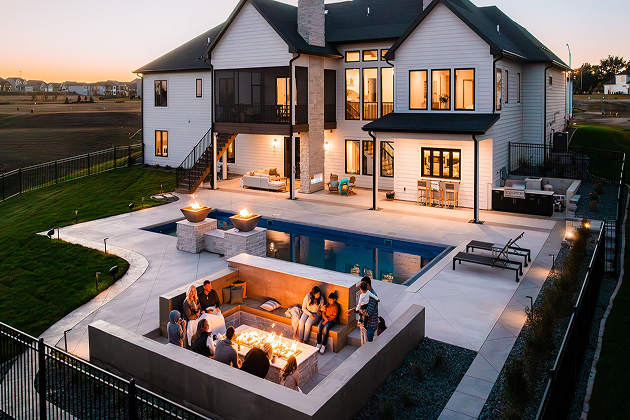 Large modern home with a backyard pool and a sunken fire‑pit seating area at dusk.
