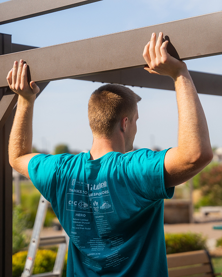 Person holding onto an overhead beam outdoors while wearing a teal T‑shirt.