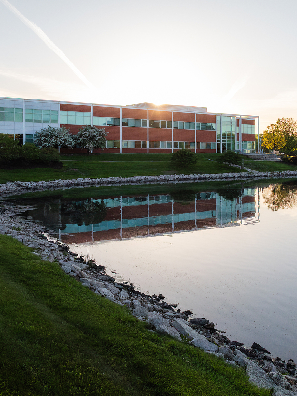 Modern office building at sunset with its reflection visible in a calm pond.