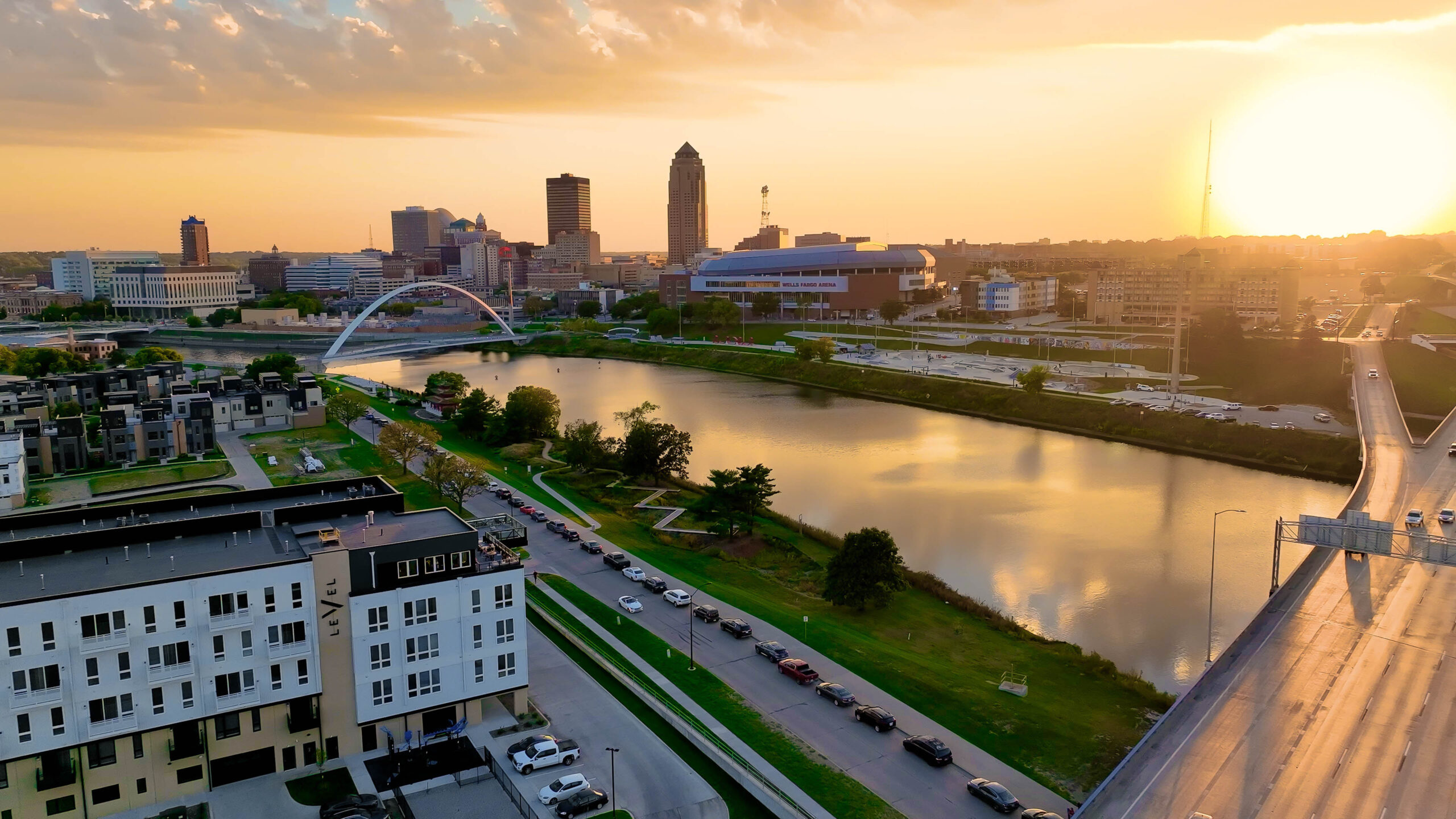 Aerial view of a city skyline at sunset with a river, bridge, and residential buildings in the foreground.