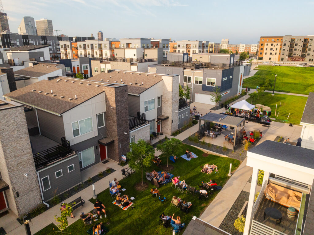 Aerial view of townhomes and apartment buildings surrounding a shared green courtyard where people are gathered.