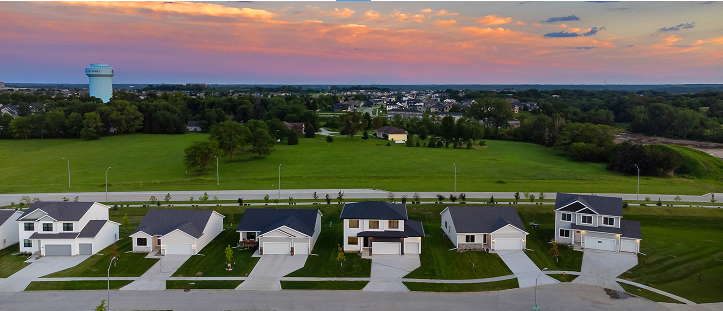 Aerial view of a row of single‑family homes facing a large open green space at sunset.