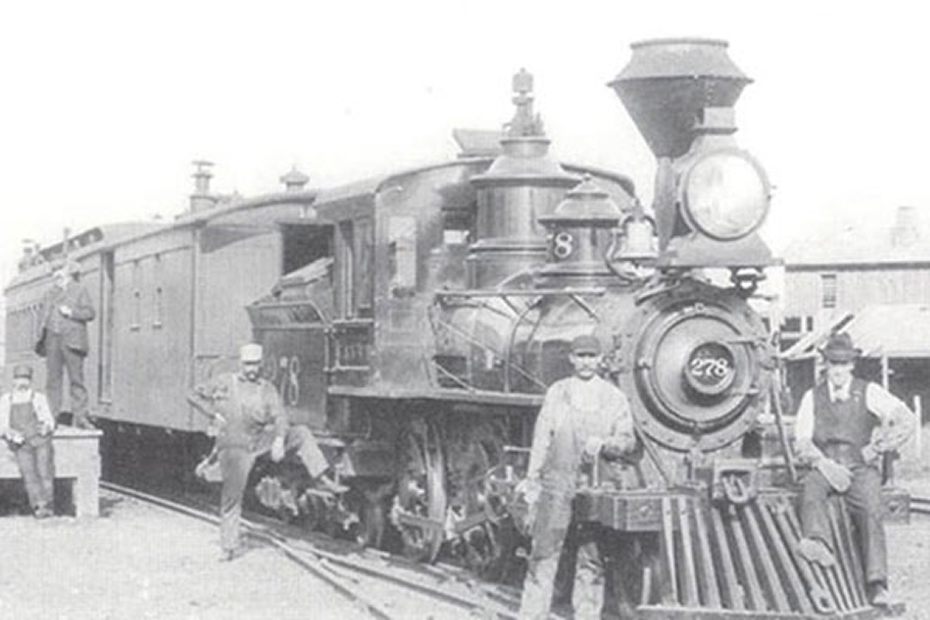 Vintage black‑and‑white photograph of a steam locomotive with several individuals standing next to the train.