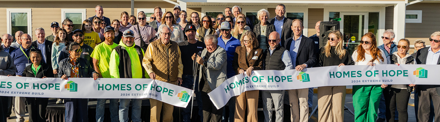 Large group holding “Homes of Hope” banners at an outdoor event for a community building project.