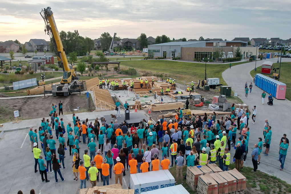 Large outdoor construction event with crews working on a building foundation while a crowd gathers nearby.