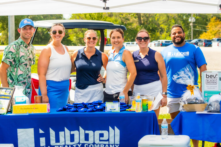 Outdoor event booth featuring branded table displays, products, and a group standing behind the table under a canopy.