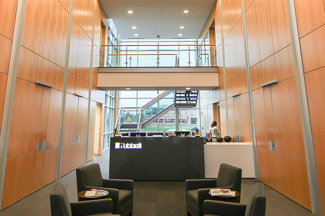 Hubbell office lobby with tall wood-paneled walls, a central reception desk, lounge chairs, and a staircase leading to an upper walkway.