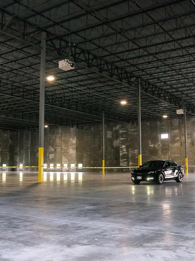 Interior of an empty warehouse with concrete floors, tall steel columns, and a dark-colored car parked inside.