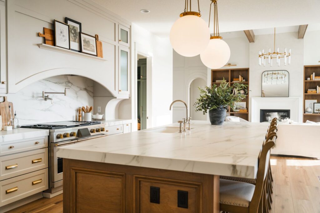 custom kitchen with range hood, large island with fireplace in background