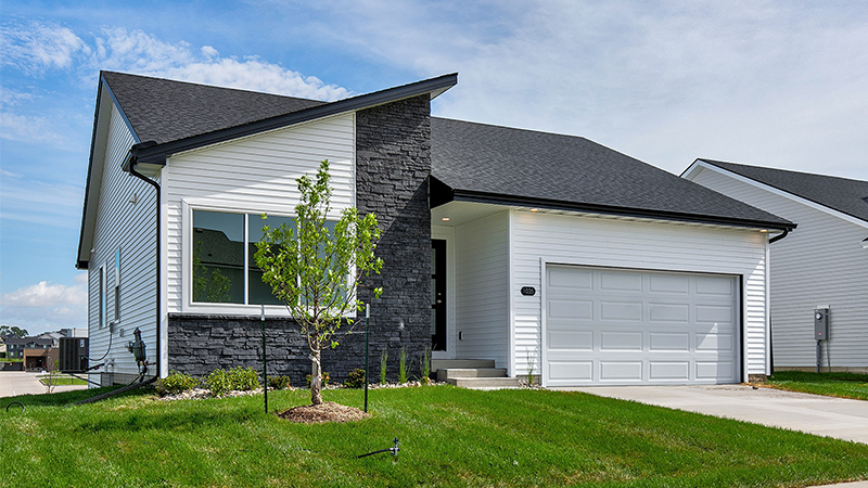Exterior of a modern white home with black stone accents and a plush green lawn