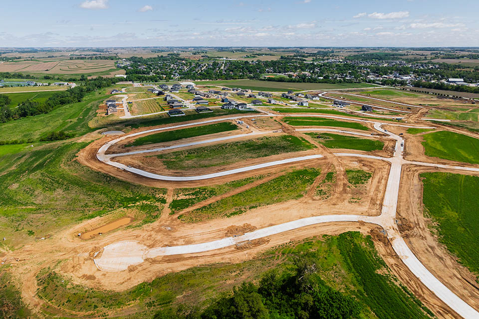 Aerial view of a residential development under construction with newly poured roads and open land.