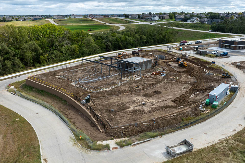 Aerial view of a construction site with steel framing, dirt work, and equipment surrounded by curved roads.