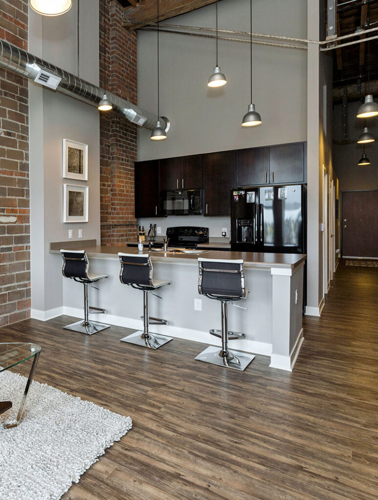 Modern loft-style kitchen with a long island, bar stools, exposed brick walls, and pendant lighting.