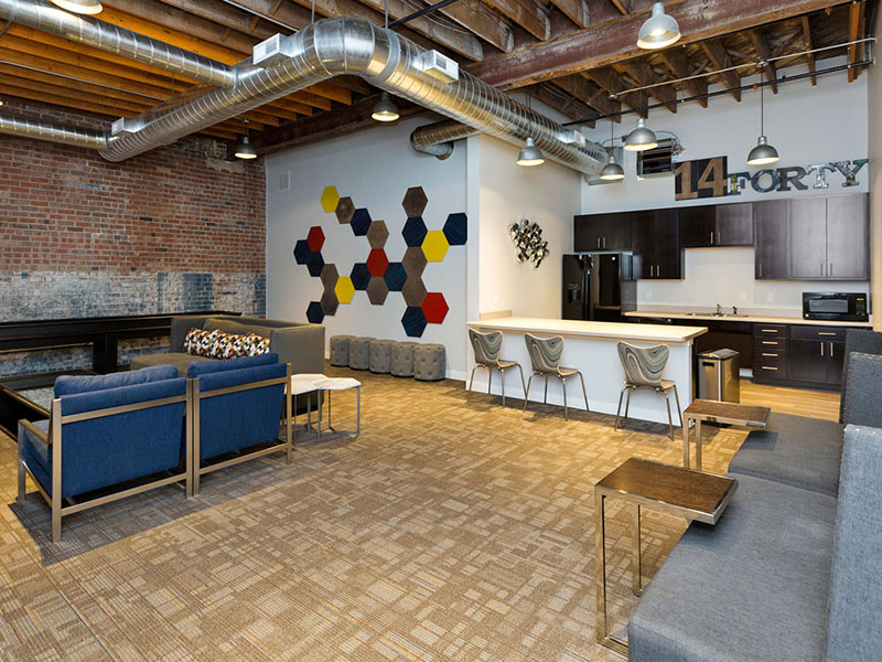 Open community lounge with seating areas, a shared kitchen, exposed brick, and industrial ceiling details.