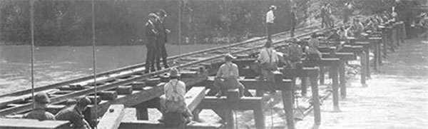 Historic 1919 photo showing workers building a wooden bridge structure over a river as part of the Des Moines Waterworks.