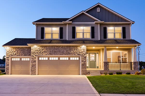 Two‑story suburban home with stone and siding exterior, three‑car garage, and a well‑lit front porch at dusk.