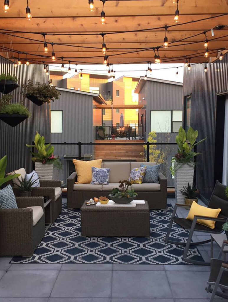 Outdoor community patio with sofas, string lights, and decorative plants between townhomes.