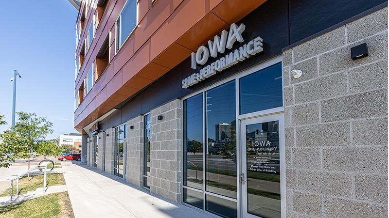 Street-level view of a modern commercial storefront labeled “Iowa Spine Performance.”