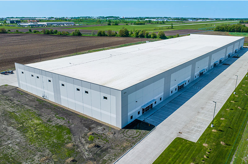 Aerial view of a large Hubbell industrial Four Mile Distribution Center with a white roof, surrounded by open fields and paved drives.