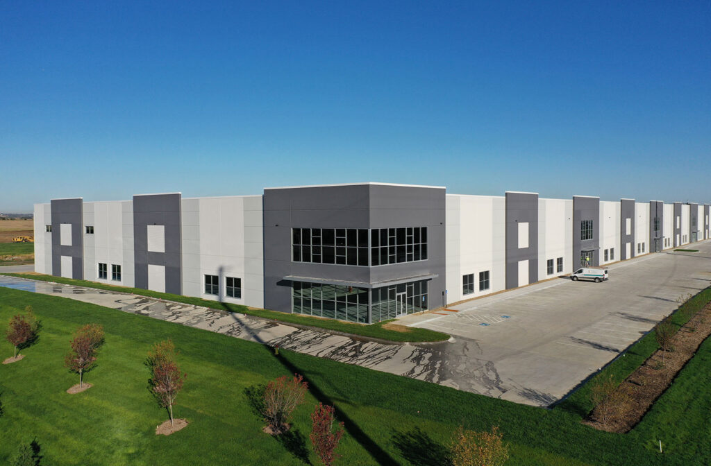 Angled exterior view of the Hubbell Infinity Industrial Center Building showing the glass‑front corner office entry and landscaped green space.