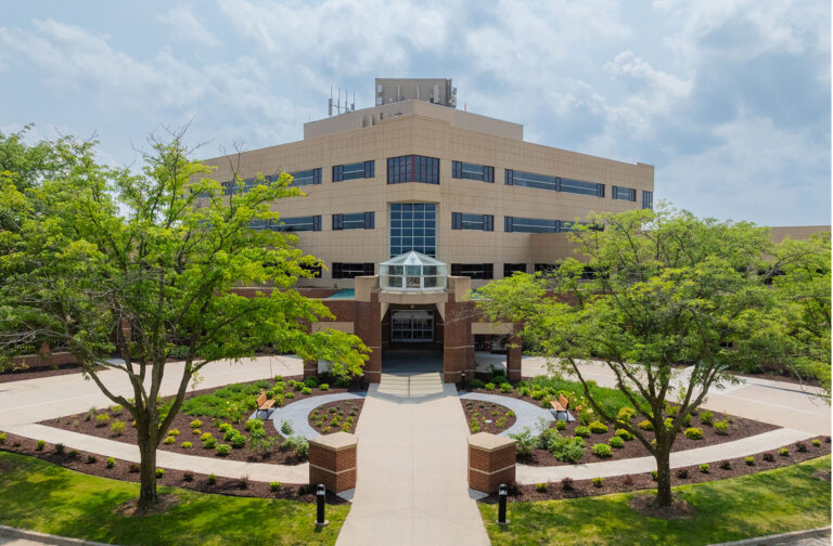 Wide exterior view of the Hubbell Lakeview Medical Park showing the main entrance with brick pillars, curved landscaping beds, and mature trees framing the building.