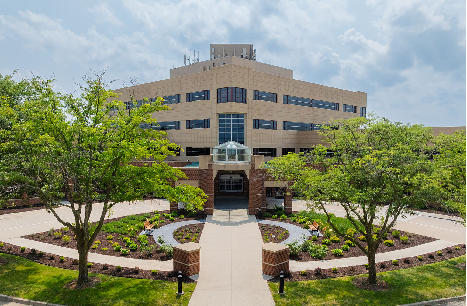 Wide exterior view of the Hubbell Lakeview Medical Park showing the main entrance with brick pillars, curved landscaping beds, and mature trees framing the building.