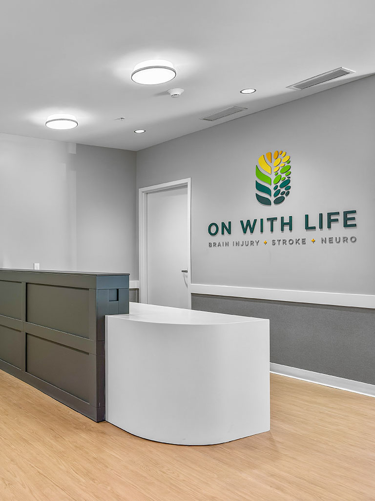 Interior reception desk of the Hubbell‑built On With Life Long Term Skilled Care Facility with the On With Life logo displayed on the wall.