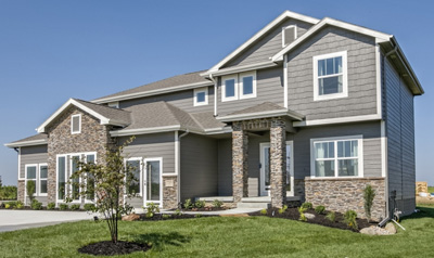 Two‑story modern home with gray siding, stone accents, large windows, and a landscaped front yard under a clear blue sky.