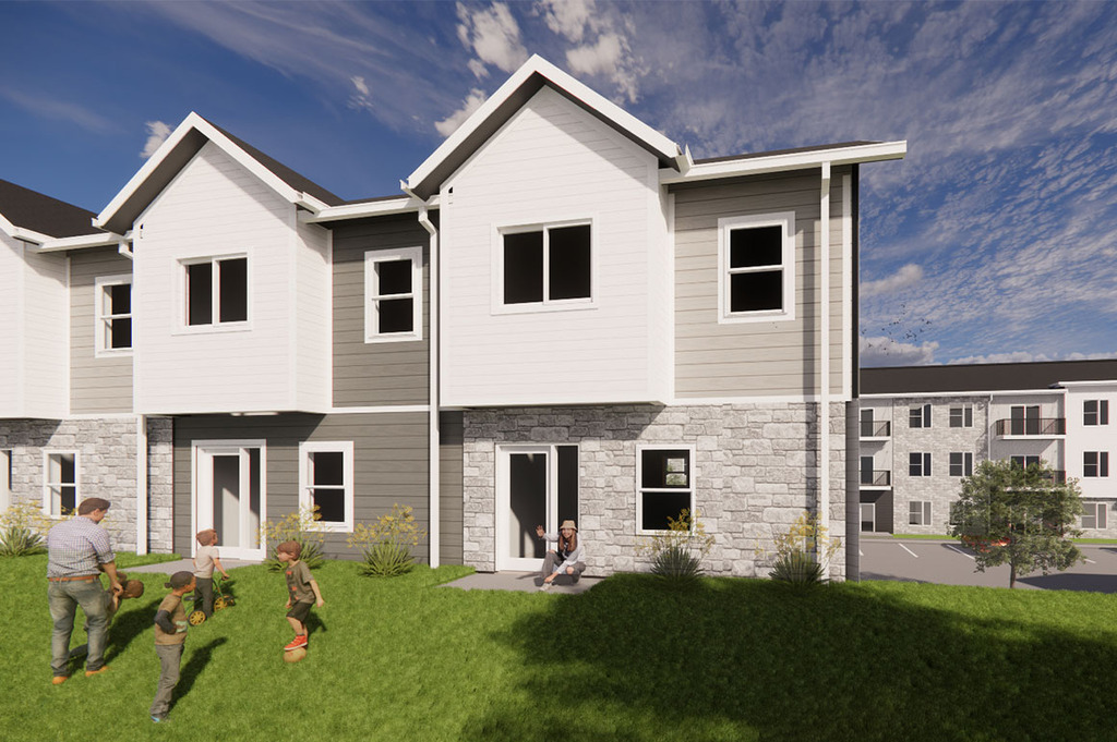 Rendering of modern two‑story townhomes with light gray siding and stone accents, with several people outside on a grassy lawn, including individuals playing and another seated near a patio door.