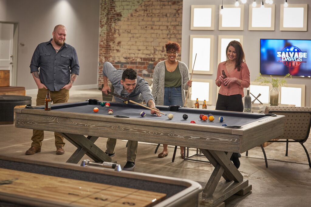 Residents gather in a community room where one person lines up a shot at a pool table while others watch and socialize in a modern shared space.