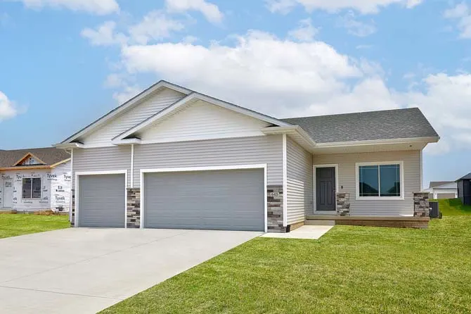Single-story rental home with light-colored siding, a two-car garage, front lawn, and a concrete driveway under a partly cloudy sky.